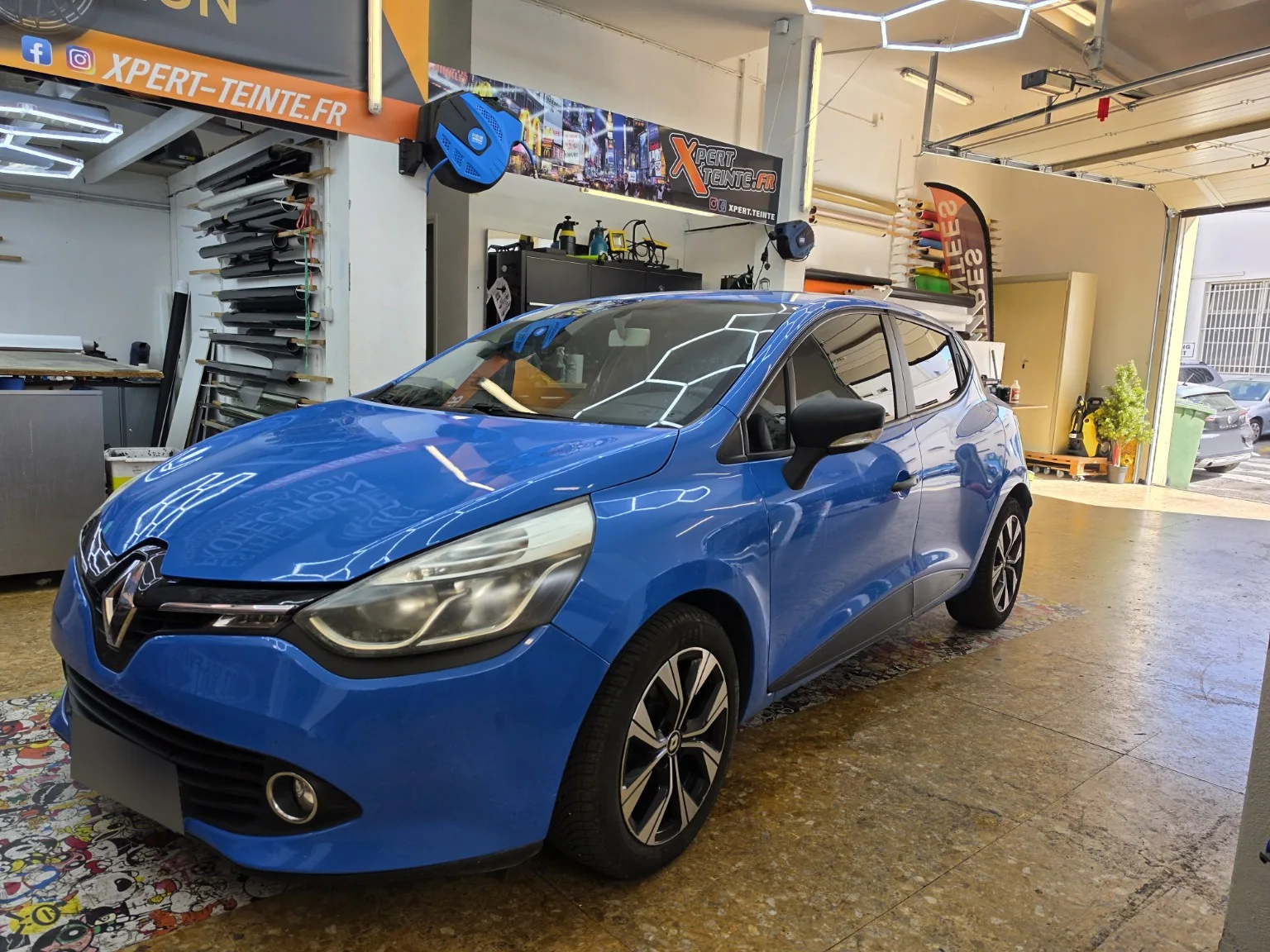 Vitres teintées Renault Clio 4 à Toulon – vue avant Vitres teintées Renault Clio 4 bleue : vue de trois quarts avant dans l’atelier Xpert Teinte à Toulon.