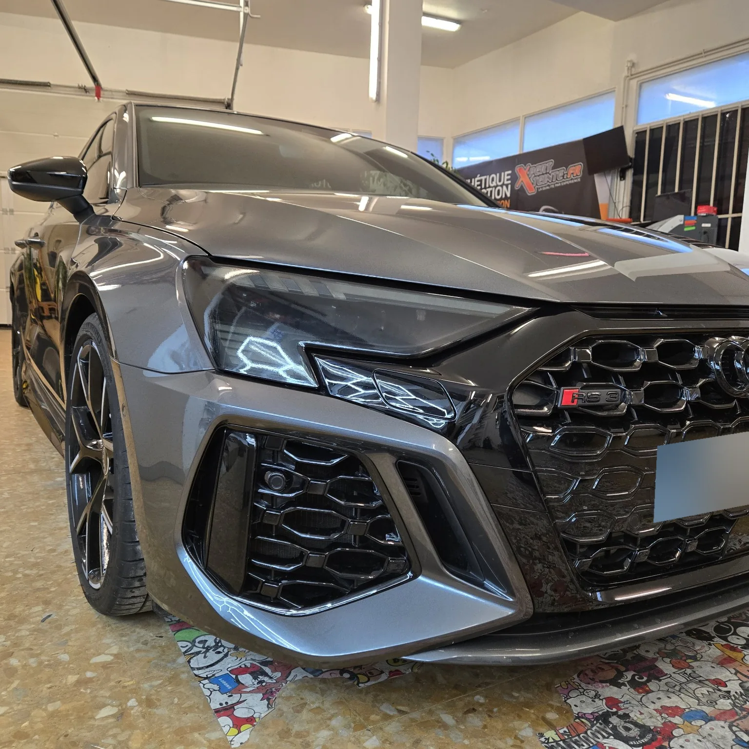 Audi RS3 – détail du phare avant teinté Gros plan sur le phare avant et la calandre de l’Audi RS3 grise chez Xpert Teinte.