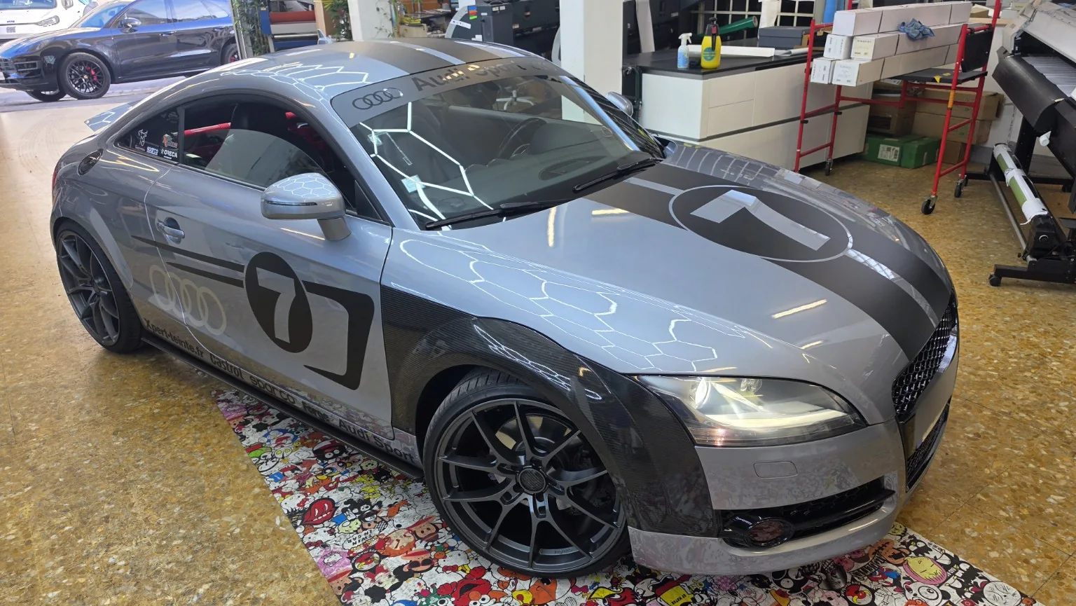 Audi TT MK2 à Toulon – kit déco carbone, noir mat et numéro 7 Audi TT MK2 grise vue de trois quarts avant, avec ailes habillées en film aspect carbone, décoration noire numéro 7 et bandeau Audi Sport.