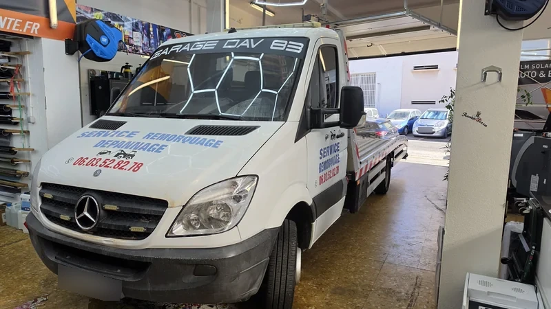 Lettrage bleu et rouge GARAGE DAV 83 sur la cabine d’une dépanneuse Mercedes blanche