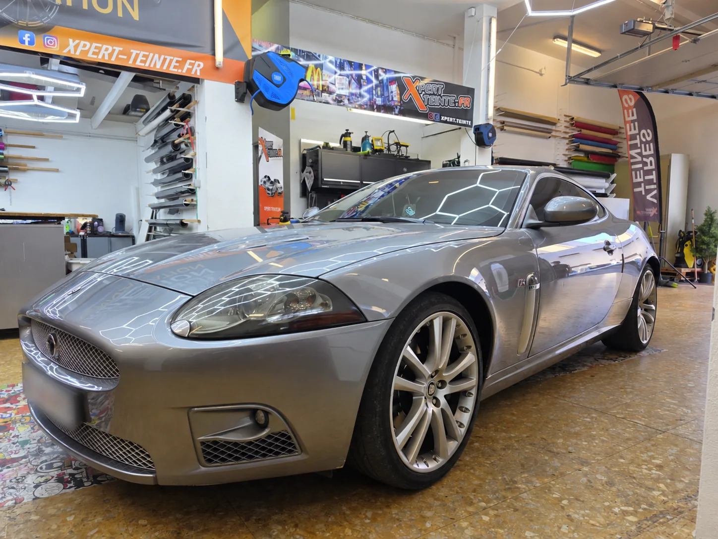Vitres teintées Jaguar XKR à Toulon – vue avant gauche Jaguar XKR grise vue de trois quarts avant gauche dans l’atelier Xpert Teinte, avec ses vitres teintées et ses phares fumés.