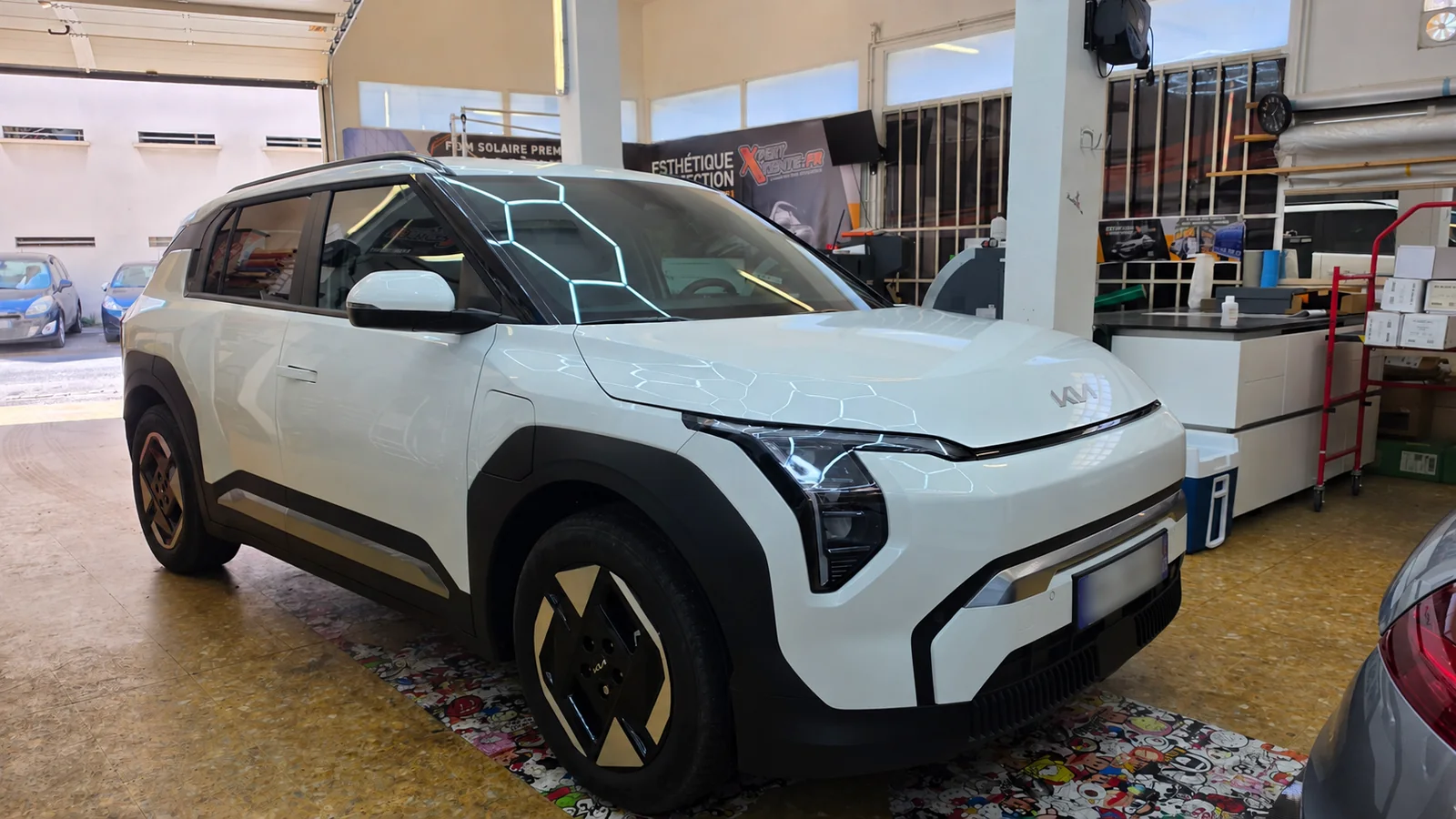 Vitres teintées Kia EV3 à Toulon – film nano-céramique Kia EV3 blanche vue de trois quarts avant droit, avec son pare-brise et ses vitrages latéraux dans l’atelier Xpert Teinte.