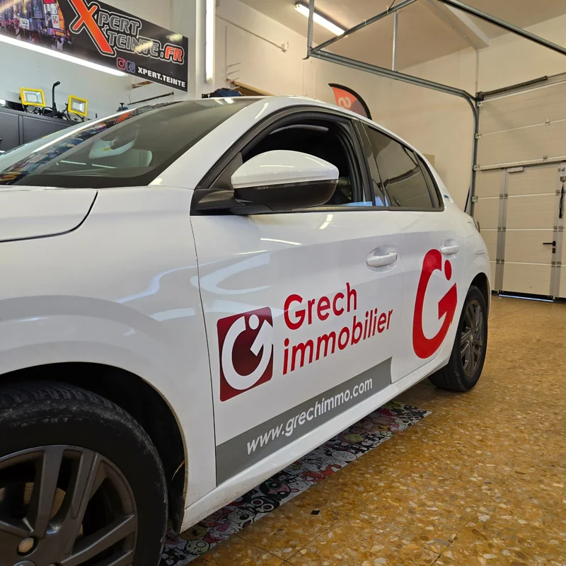 Logo rouge et nom Grech immobilier sur la portière d’une voiture blanche