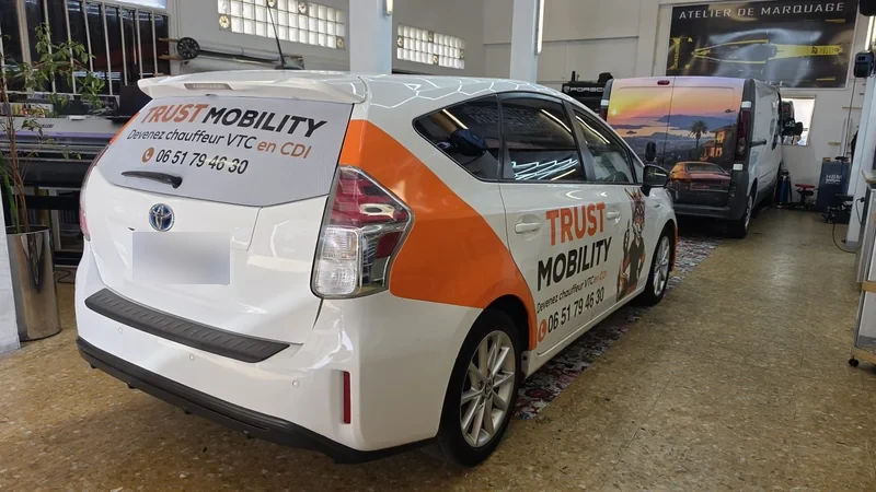 Marquage orange et noir TRuST Mobility sur une voiture Toyota blanche, vue arrière trois quarts