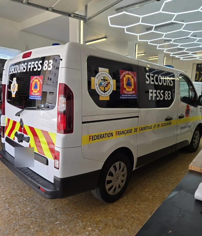 Bandes jaunes et rouges et identification FFSS 83 à l’arrière d’un Renault Trafic blanc