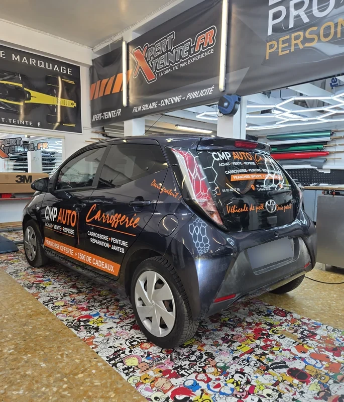Lettrage blanc et orange CMP AUTO sur une Toyota Aygo sombre