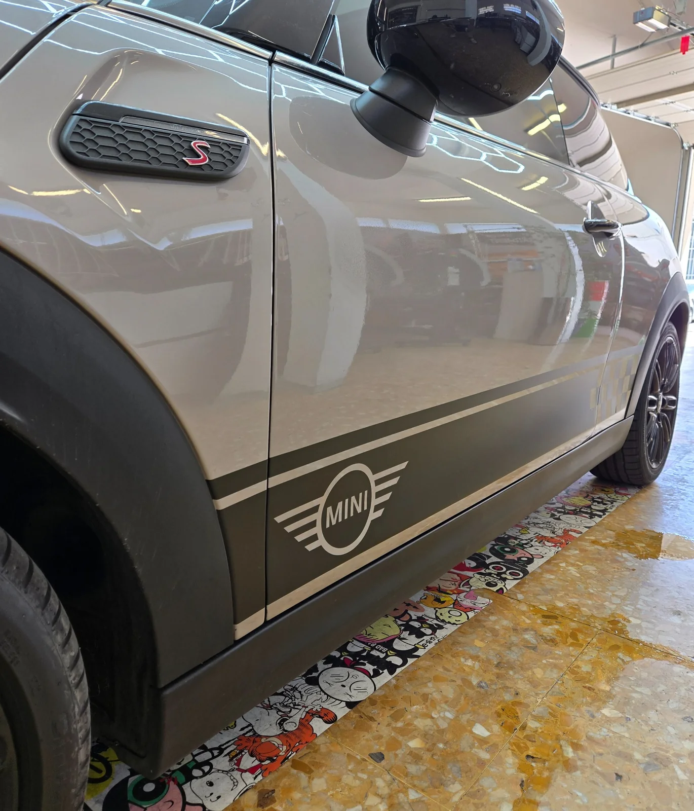 MINI Cooper S – bandes de bas de caisse noir mat sur mesure Détail des bandes adhésives noir mat, du motif MINI et du damier sur le bas de caisse d’une MINI Cooper S.