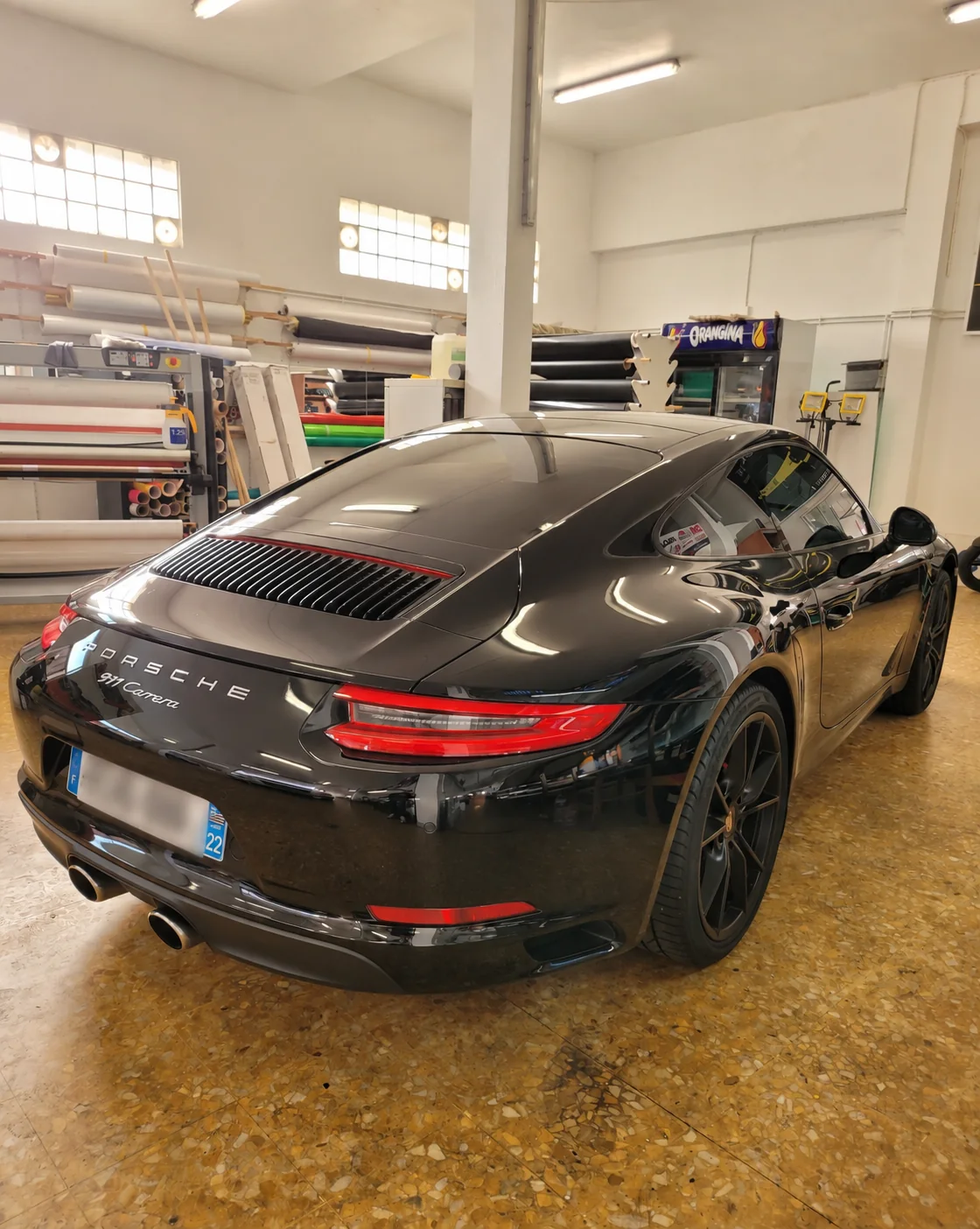 Film de discrétion Porsche 911 Carrera à Toulon – arrière Vue arrière de la Porsche 911 Carrera noire avec sa lunette teintée, sa custode et les reflets de l’atelier.