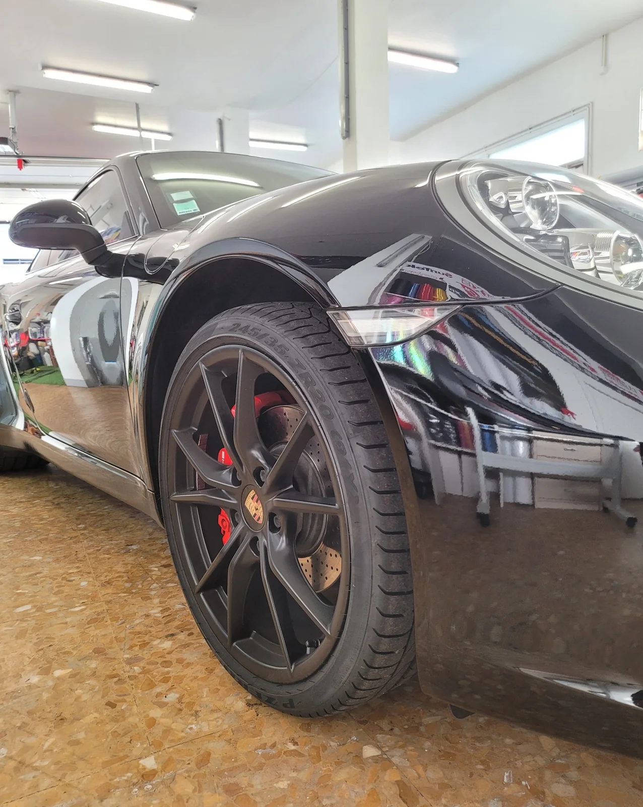 Porsche 911 Carrera noire à Toulon – détail de carrosserie Gros plan de la roue avant, de l’aile et du phare de la Porsche 911 Carrera noire dans l’atelier.